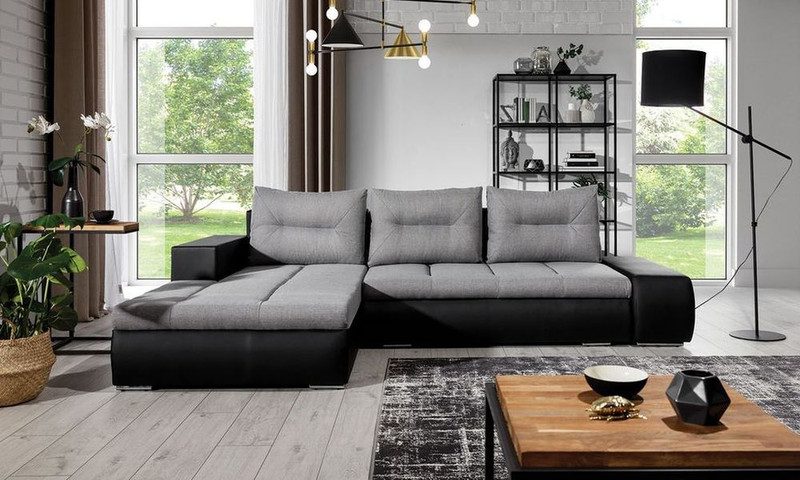Foxglove corner sofa bed with grey fabric seat and back cushions on a black leather-look base, chaise on the left, beside a wooden coffee table and a black floor lamp