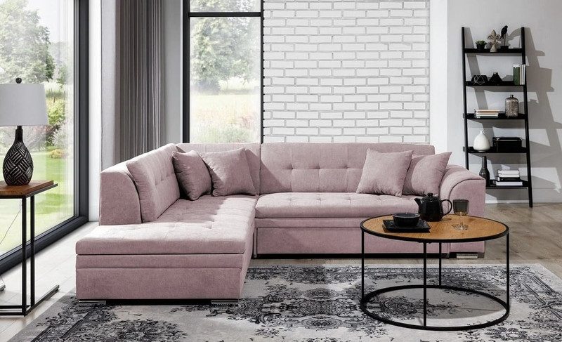 Blush pink Everleigh corner sofa bed with the chaise on the left, matching cushions, a round oak-top coffee table and a grey patterned rug in front