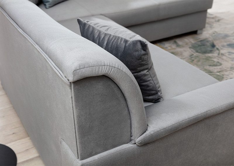 Close-up of the rounded arm and seat of a light grey Mistral corner sofa bed with a dark grey scatter cushion