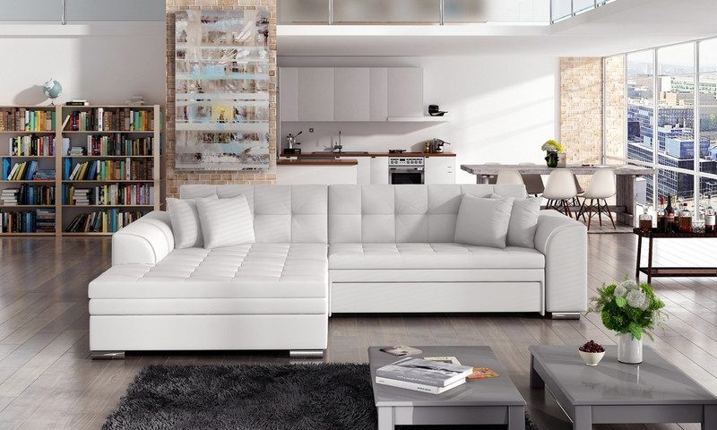 White eco leather Rosslyn corner sofa bed with quilted seats and the chaise on the left, in an open-plan loft with bookshelves, a kitchen behind and two grey coffee tables