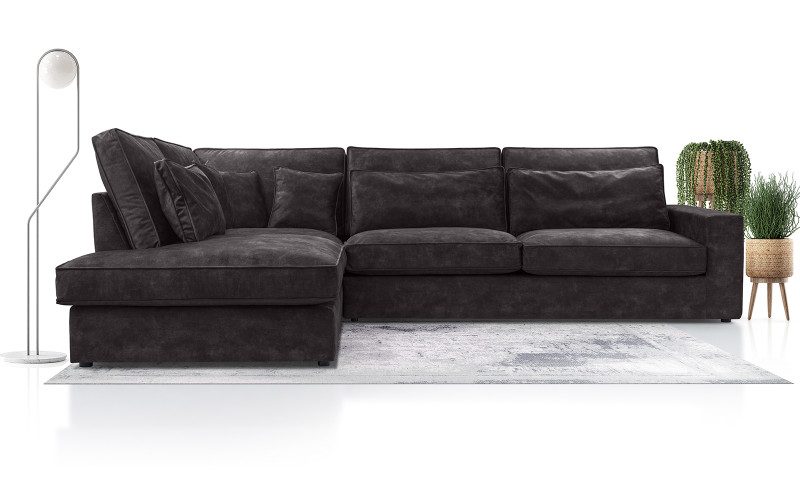 Nolan Cozy corner sofa bed in dark grey with deep seat and back cushions and the chaise on the left, on a pale rug beside a floor lamp and potted plants