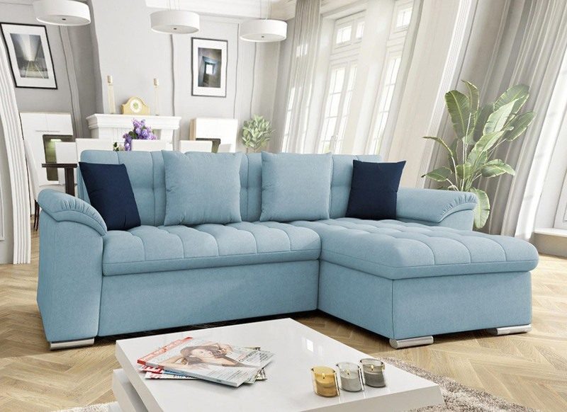 Light blue Goldcrest Mini corner sofa bed with navy cushions in a bright living room, with a white coffee table in the foreground