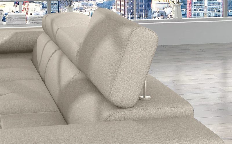 Close-up of a cream Hollingwood Mini corner sofa bed with one headrest raised on its metal support, by a large window