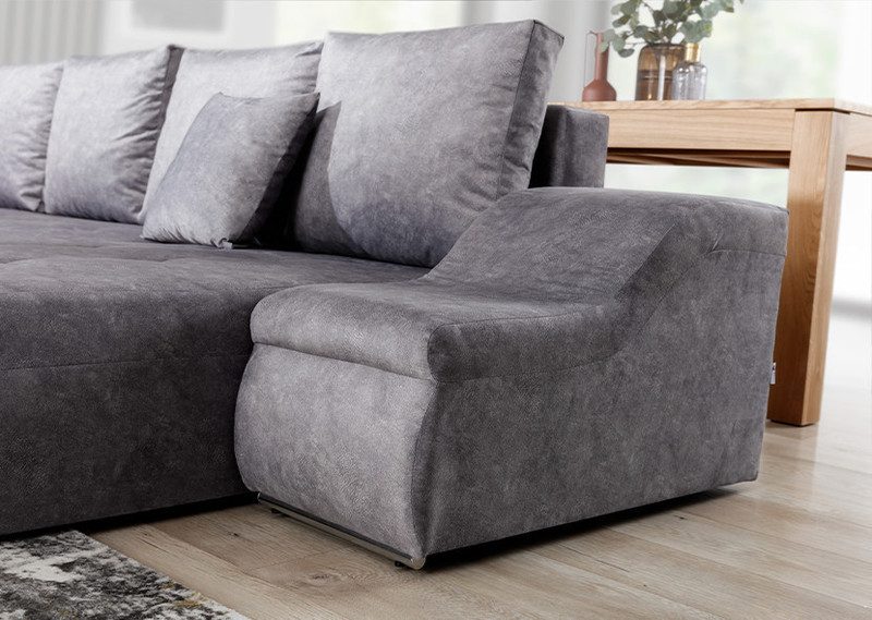 Close-up of the grey textured fabric on the arm and chaise end of a Zephyra U-shaped sofa bed, with a light wood floor