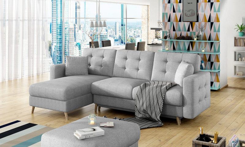 Light grey Merrow corner sofa bed with a buttoned back and the chaise on the left, styled with grey scatter cushions and a black and white throw on a pale wood floor