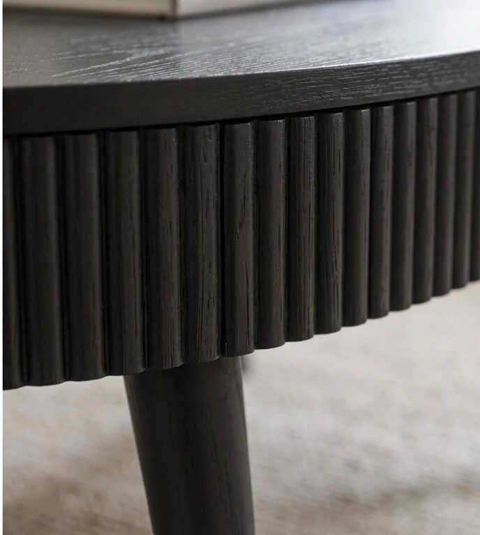 Close-up of a round Selborne dark oak drum coffee table with a fluted tambour side and tapered leg on a light rug